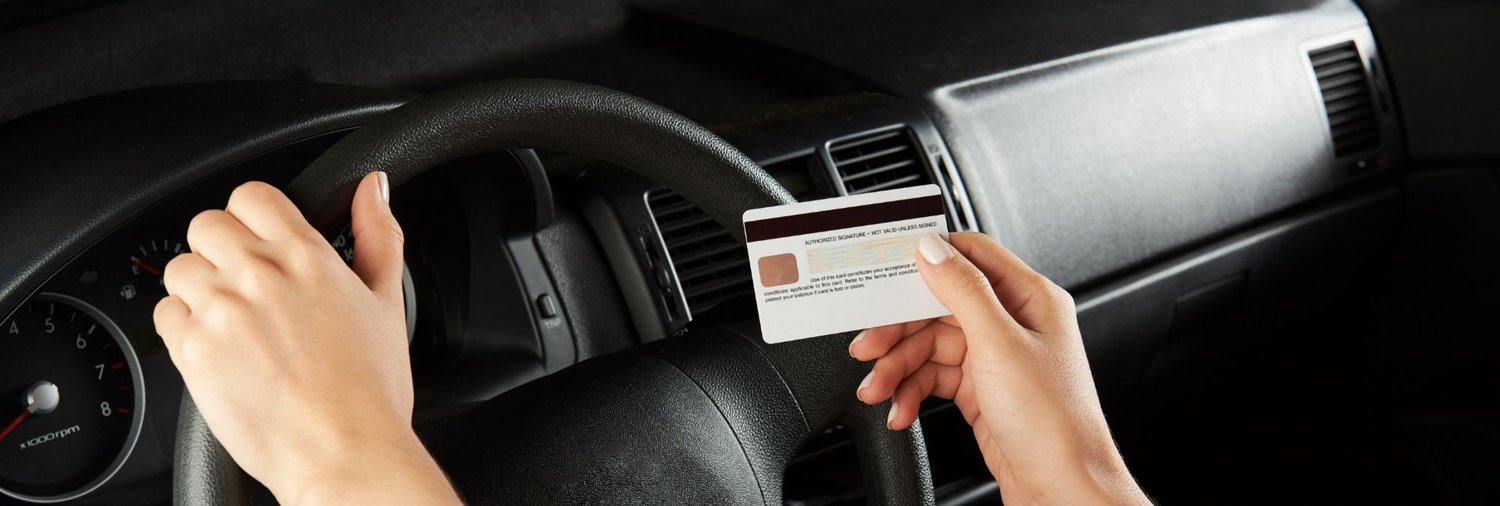 women's hands in a car, one on the steering wheel, one holding a credit card