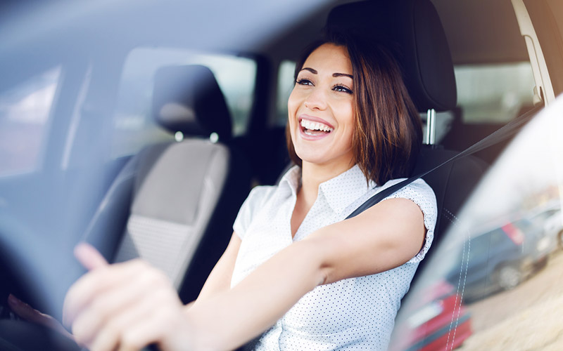 Woman with dark brown hair appearing to laugh as she is driving