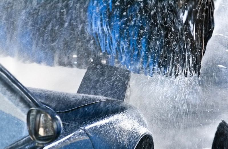 a blue car with pop up headlight approaching a brush within the car wash