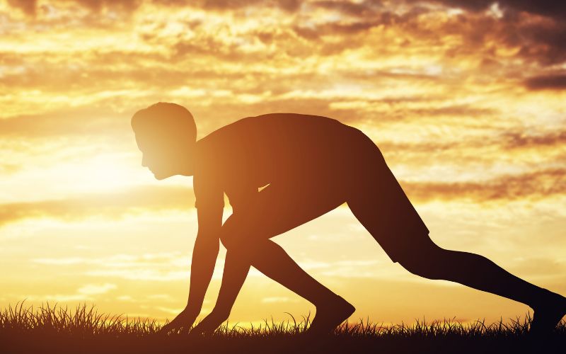 man crouched down as if he's about to start a race in the sunrise