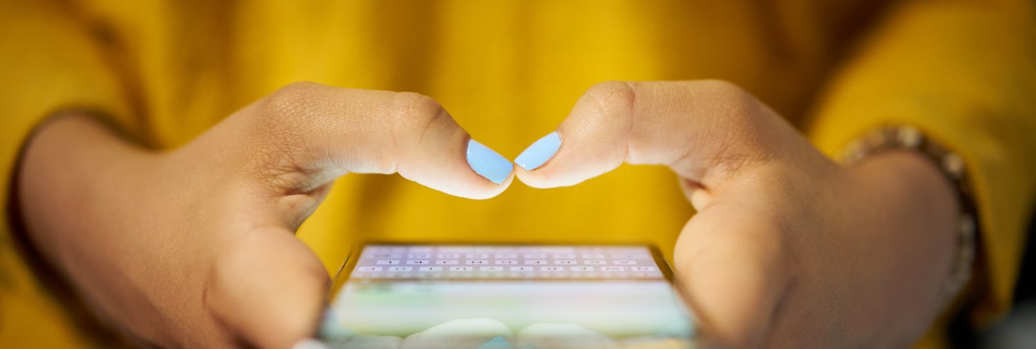 close up of a person's thumbs tapping on a smartphone screen with a yellow sweater as a background