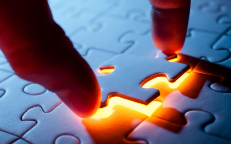 a hand placing a puzzle place into a glowing empty spot on a puzzle