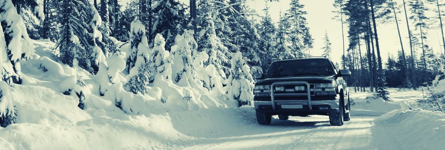 black pickup truck driving on a snowy road surrounded by snow-covered trees