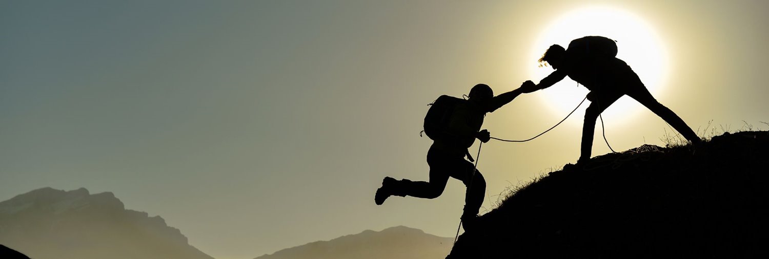 silhouette of a climber helping another to the peak of a mountain