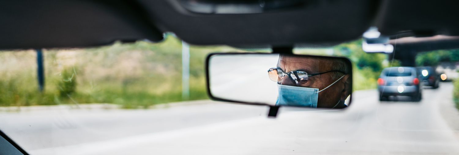 reflection in rear view mirror of a man wearing a mask