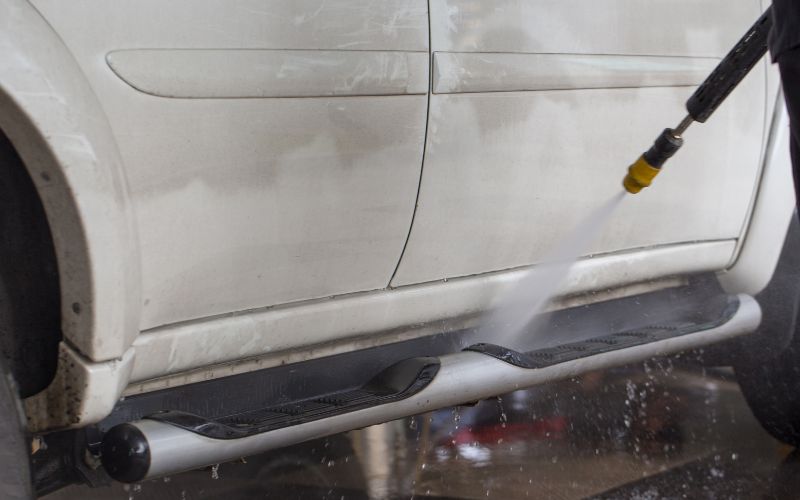 bottom of white car being sprayed by a car wash prep gun