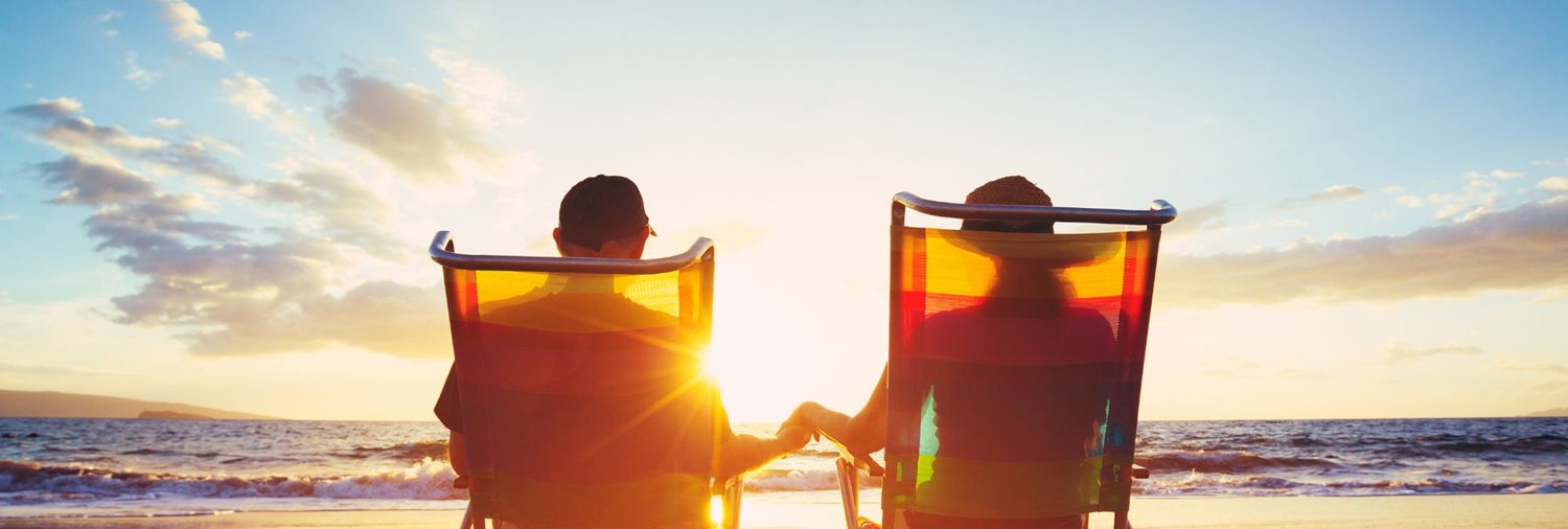 couple sitting on beach in beach chairs holding hands watching the sunset