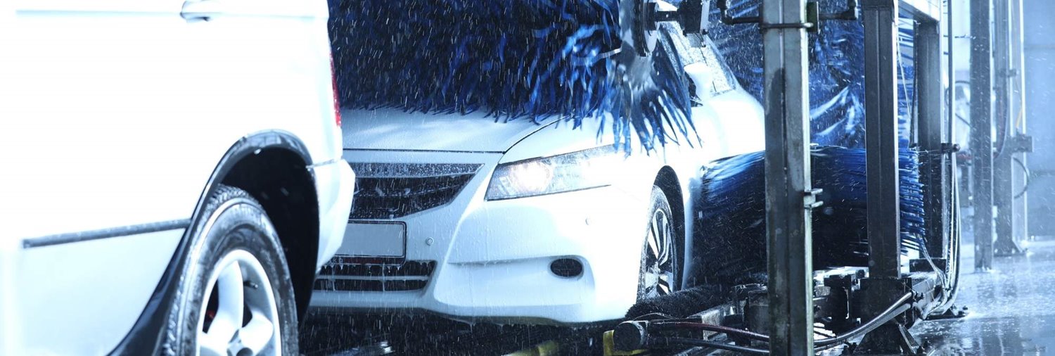 white sedan going through car wash as top wrap cleans the hood 