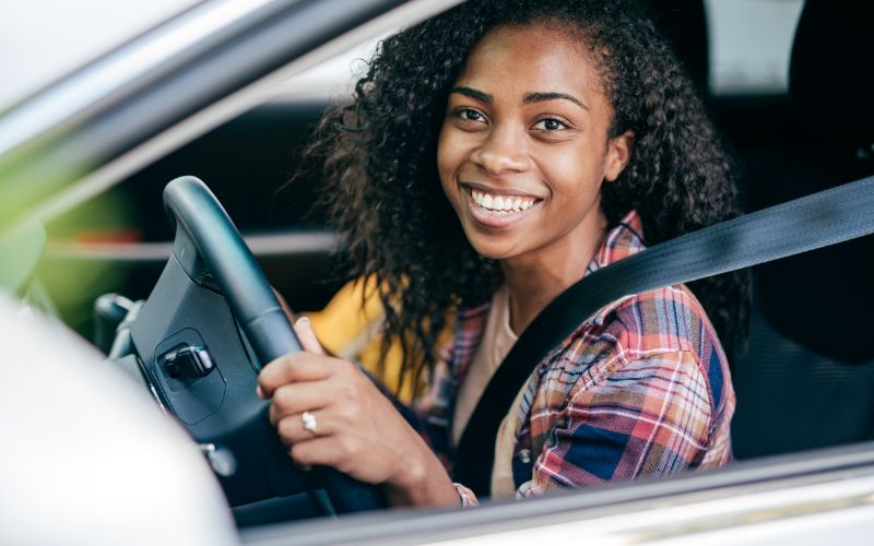 woman in car holding on to steering wheel and smiling