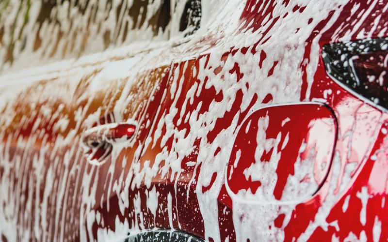 closeup of the side of a red car with soap suds dripping down it