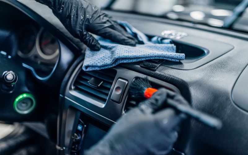 gloved hands using a brush on a car's air vents