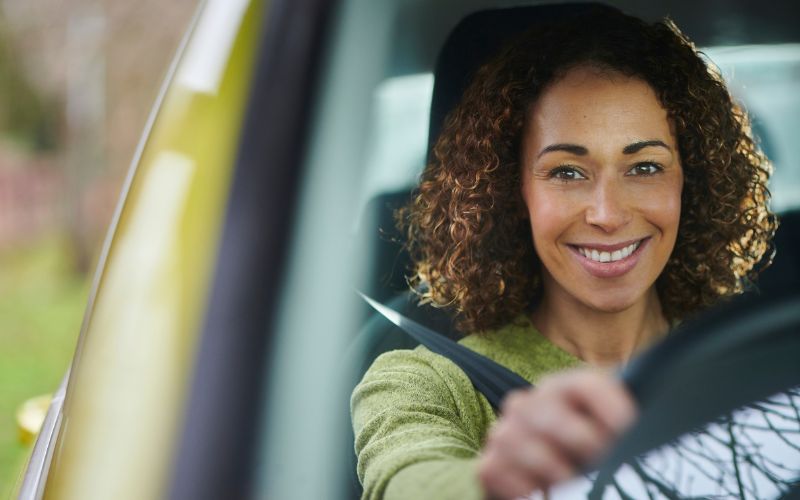 woman smiling behind wheel of car