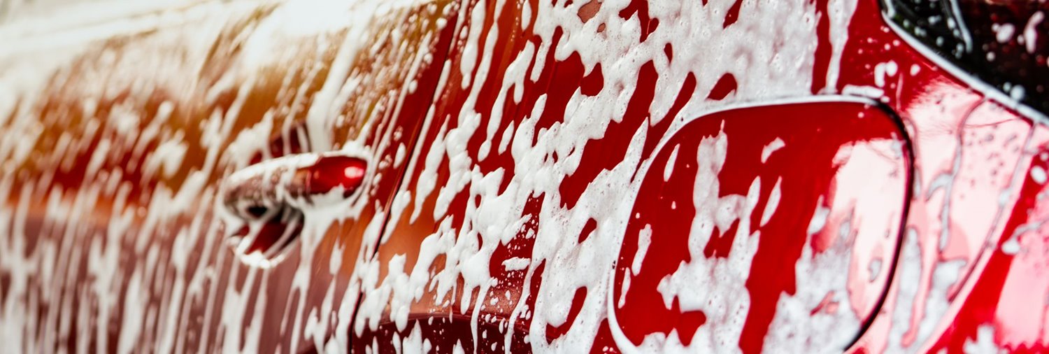 closeup of the side of a red car with soap suds dripping down it