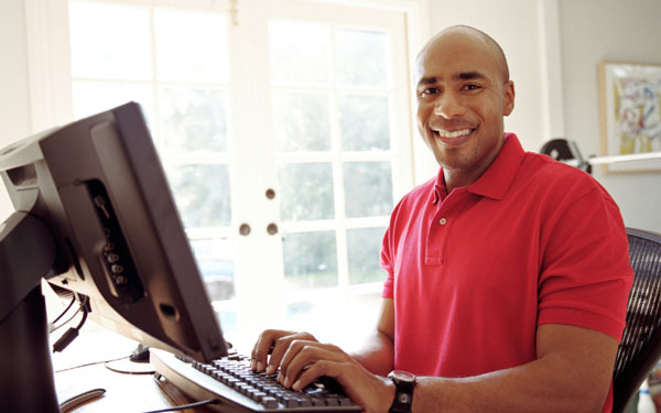 man in a red golf shirt typing on a computer in his home office