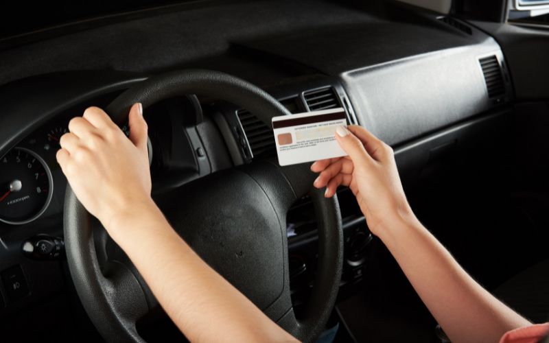 women's hands in a car, one on the steering wheel, one holding a credit card