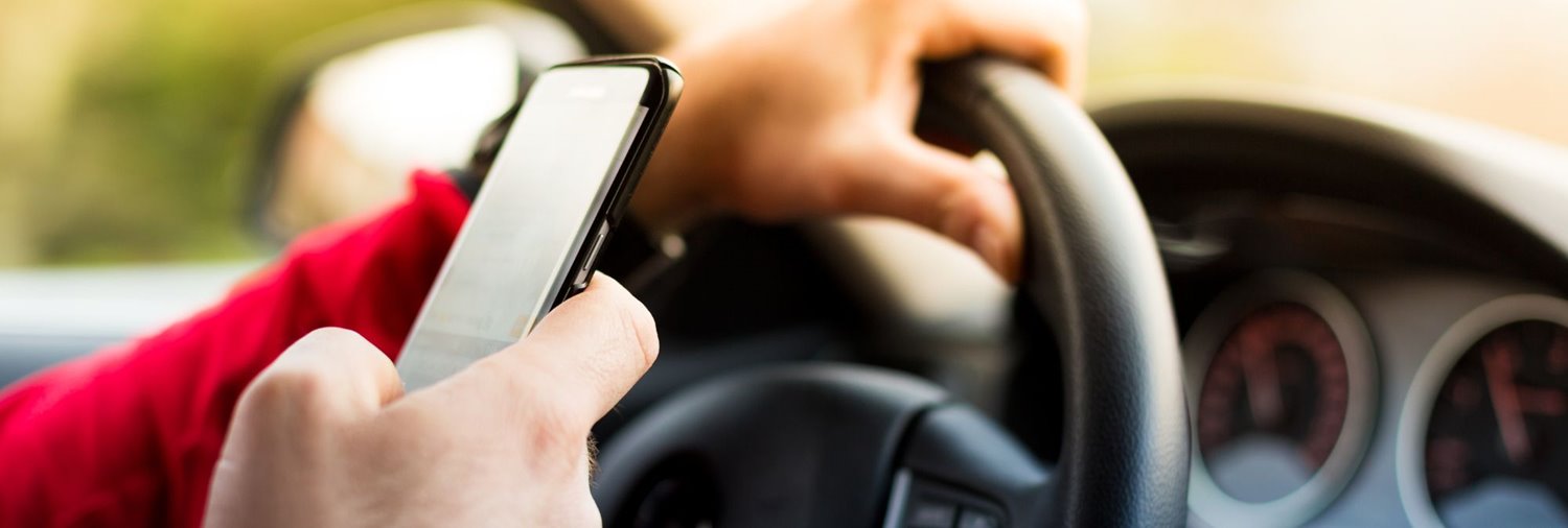 a persons hands, one holding a car wheel and the other gripping a phone