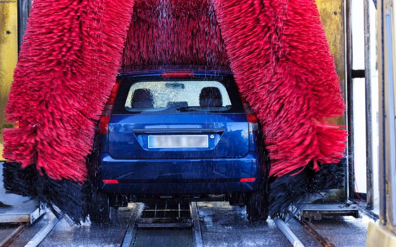rear of a blue car inside a running in-bay automatic car wash