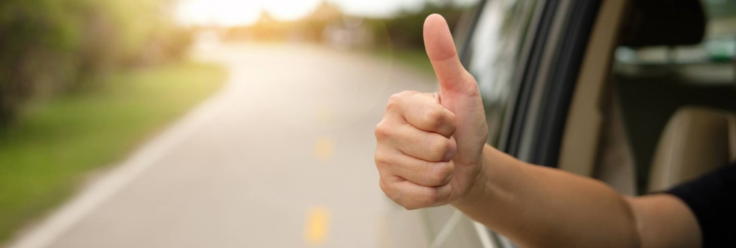 close up of someone giving a thumbs up outside a vehicle going down the road