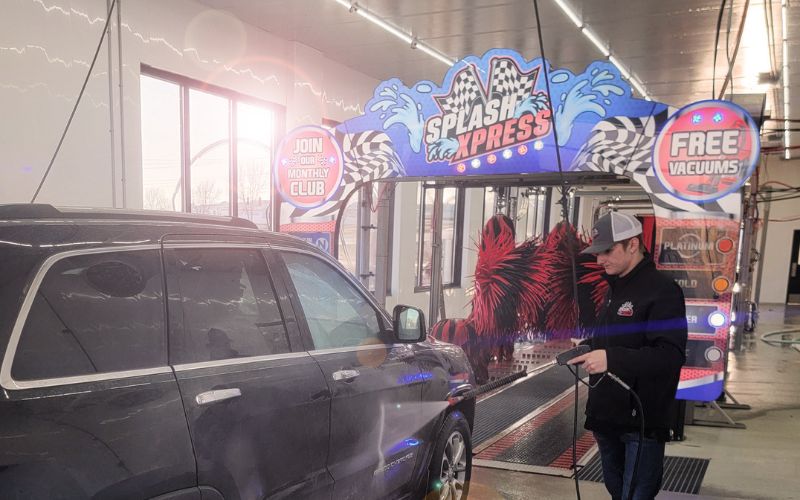car wash attendant spraying a vehicle as it enters the car wash tunnel