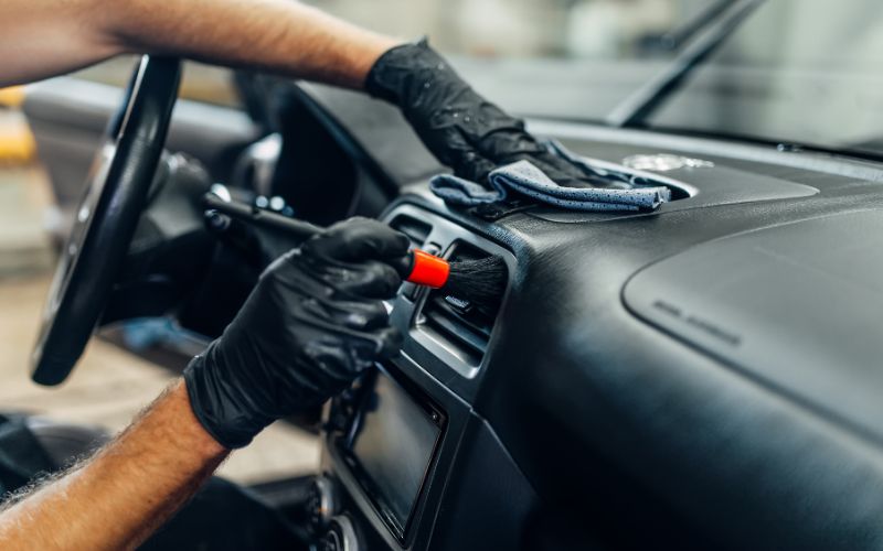gloved hands brushing out a car air vent at a full service car wash