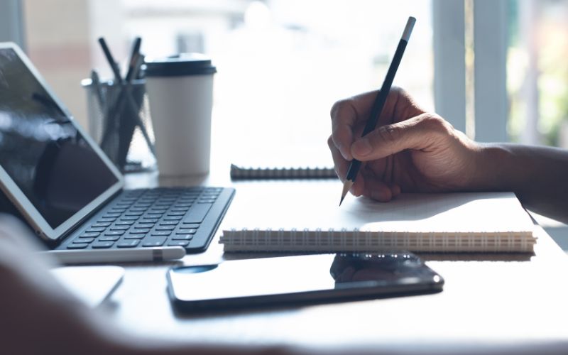 person taking notes in front of a laptop