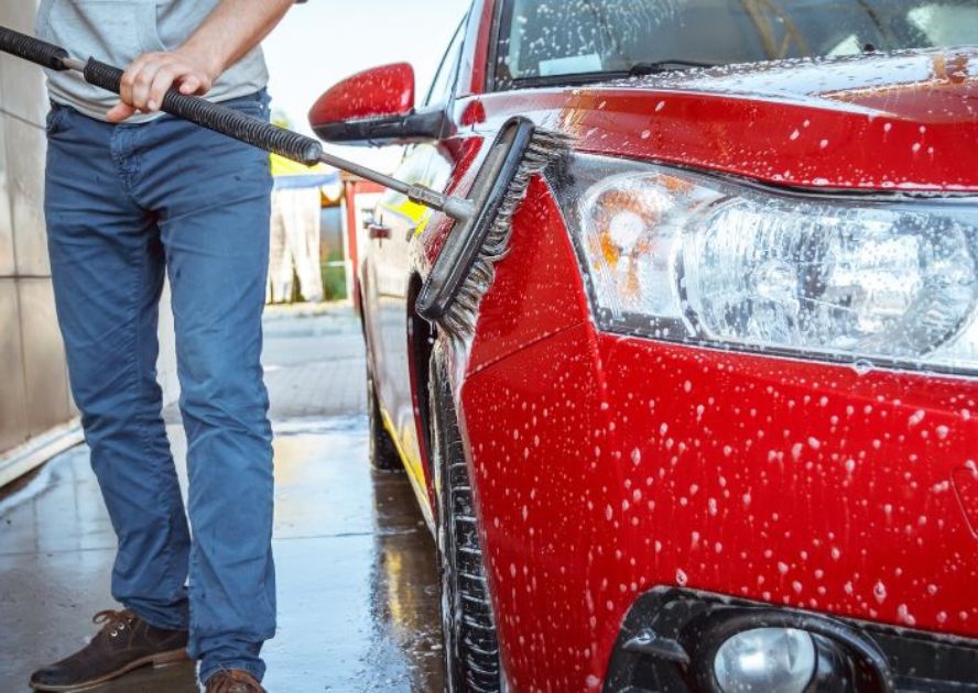 someone using a brush in a self-serve car wash on a red car