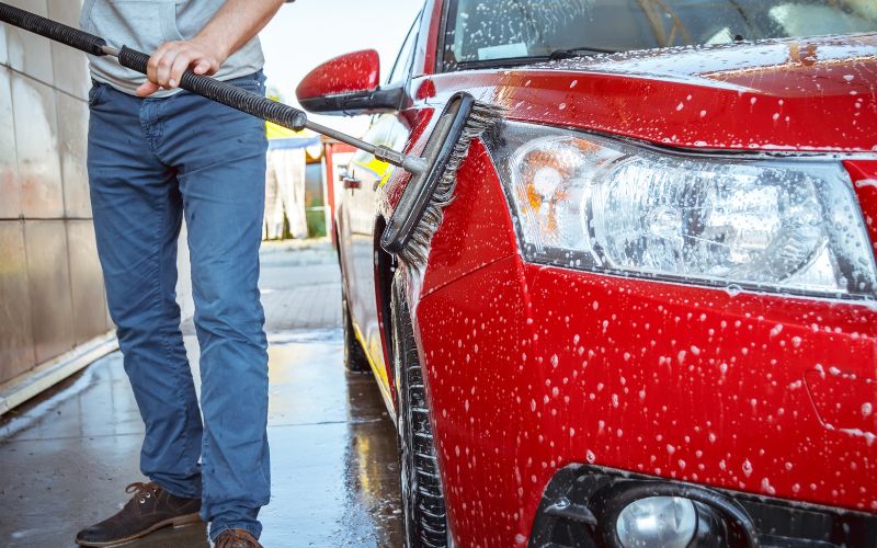 shot of lower half of man washing red car with a brush in a self service car wash
